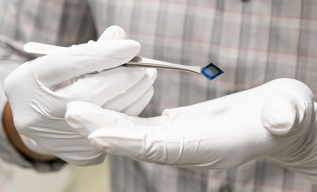 Gloved hands holding tweezers and a computer chip